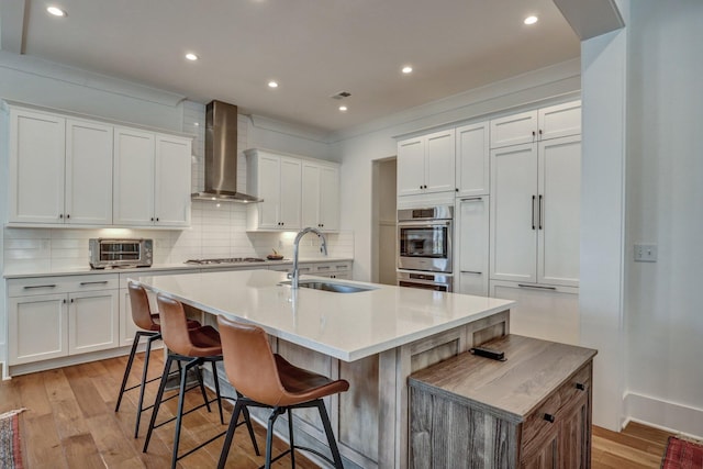 kitchen featuring a sink, wall chimney range hood, a toaster, light wood finished floors, and decorative backsplash