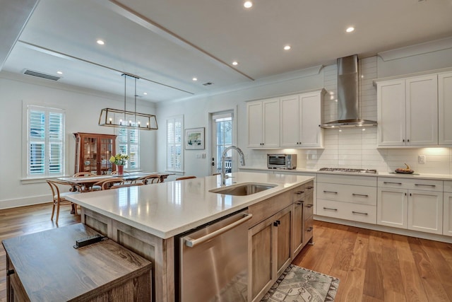 kitchen featuring visible vents, a sink, stainless steel appliances, wall chimney range hood, and decorative backsplash