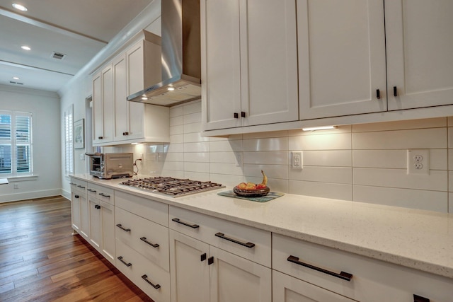 kitchen featuring backsplash, wall chimney range hood, stainless steel gas cooktop, a toaster, and light wood-type flooring