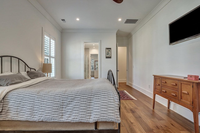 bedroom featuring visible vents, baseboards, wood finished floors, and ornamental molding