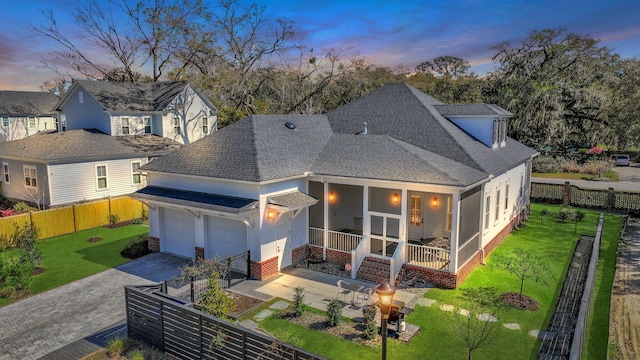 back of house featuring driveway, a yard, a sunroom, a shingled roof, and fence private yard