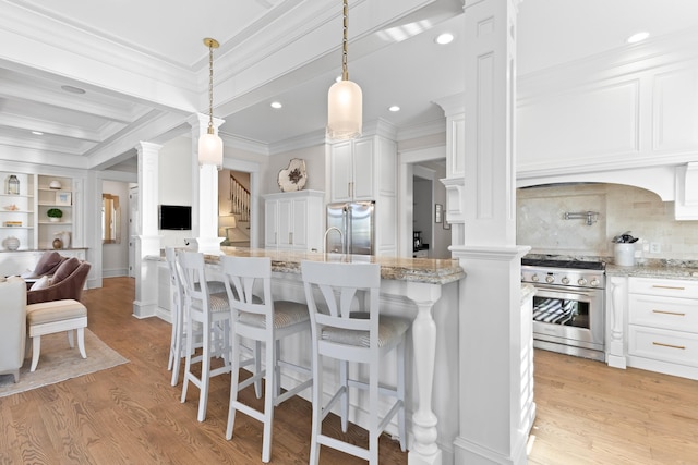 kitchen featuring light wood finished floors, appliances with stainless steel finishes, ornamental molding, and decorative columns