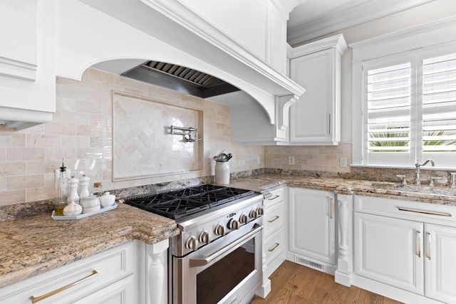 kitchen with stainless steel range, custom exhaust hood, backsplash, and white cabinets