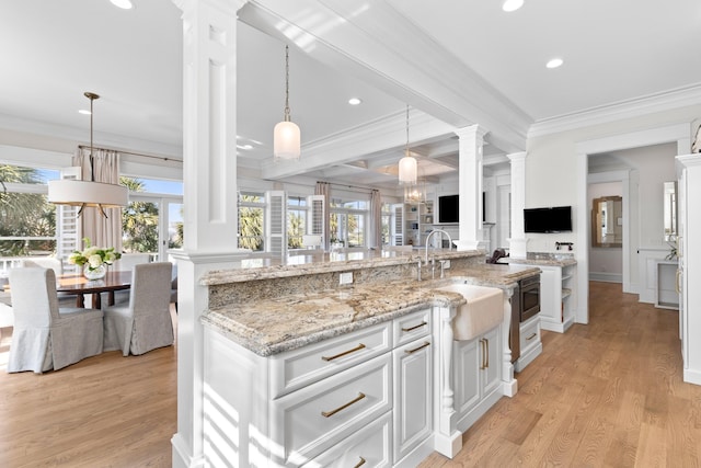 kitchen featuring crown molding, light wood-style floors, a sink, and decorative columns