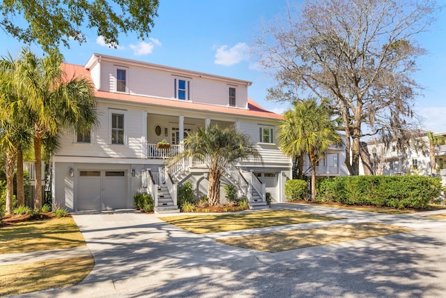 raised beach house with a garage, covered porch, driveway, and stairs