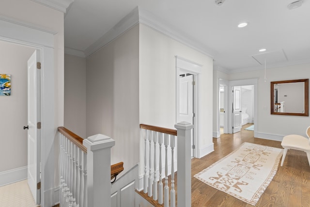 corridor featuring wood finished floors, an upstairs landing, baseboards, ornamental molding, and attic access