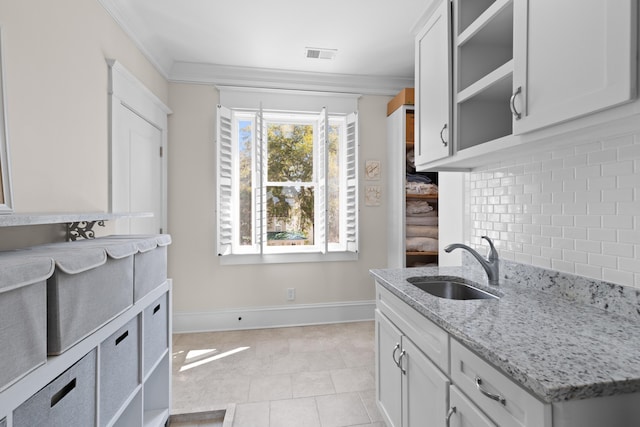 kitchen with visible vents, baseboards, decorative backsplash, light stone countertops, and a sink