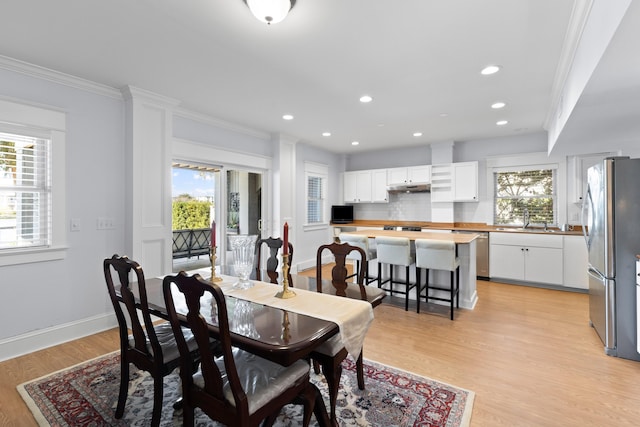 dining area with light wood finished floors, a healthy amount of sunlight, and crown molding