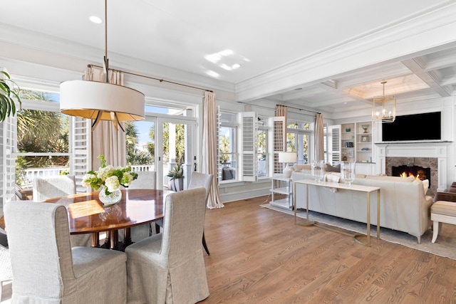 dining room featuring a wealth of natural light, beamed ceiling, a lit fireplace, and wood finished floors