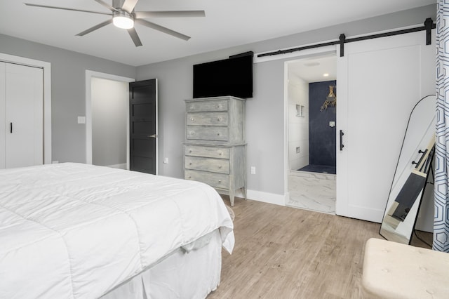 bedroom featuring a barn door, baseboards, ensuite bath, ceiling fan, and light wood-style flooring