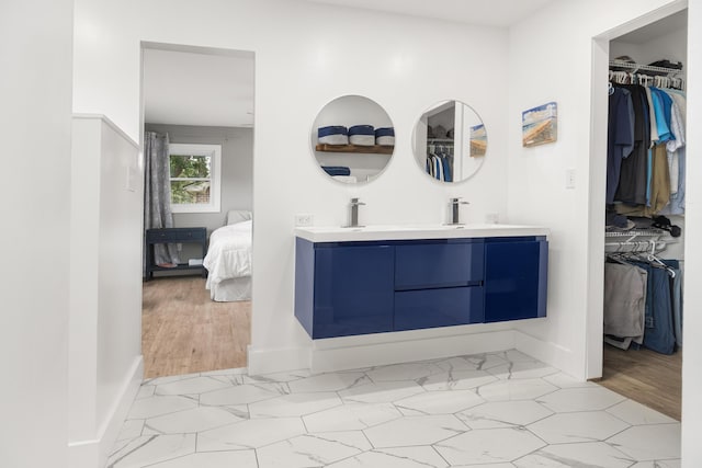 bathroom with connected bathroom, a spacious closet, double vanity, and baseboards