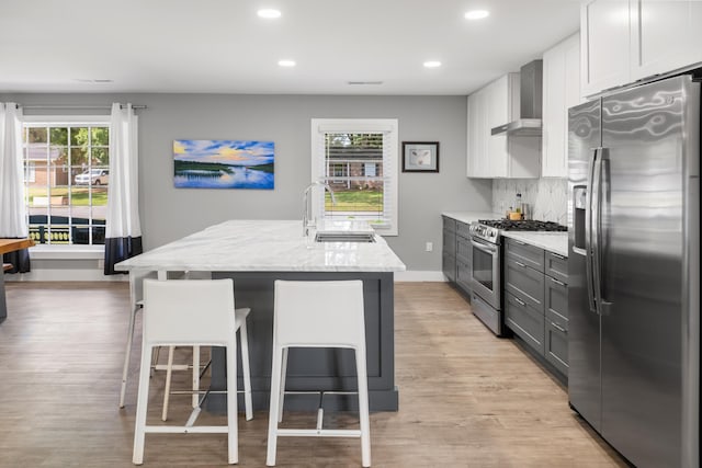 kitchen featuring appliances with stainless steel finishes, a sink, a breakfast bar area, light stone counters, and wall chimney exhaust hood
