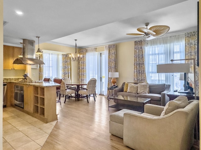 living area with light wood finished floors, plenty of natural light, ornamental molding, and ceiling fan with notable chandelier