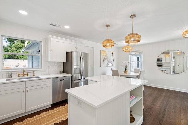 kitchen with sink, appliances with stainless steel finishes, white cabinetry, hanging light fixtures, and a center island