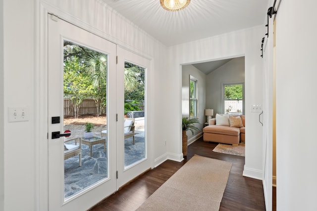 doorway to outside with dark wood-type flooring, a barn door, and vaulted ceiling