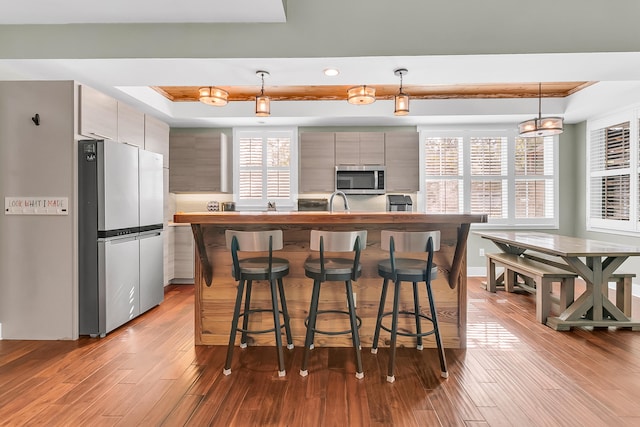 kitchen featuring a healthy amount of sunlight, pendant lighting, appliances with stainless steel finishes, and light hardwood / wood-style flooring