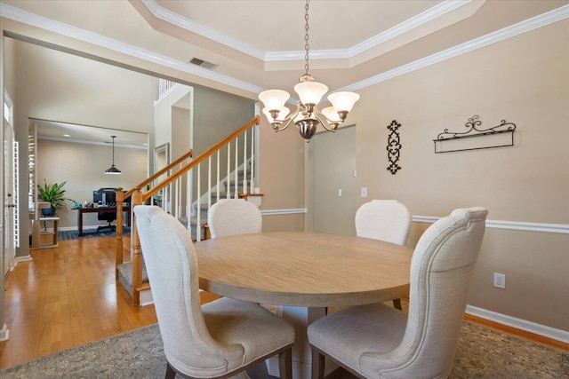 dining room featuring visible vents, a tray ceiling, stairs, light wood-type flooring, and a chandelier