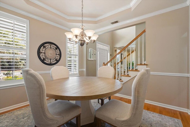 dining area with a raised ceiling, an inviting chandelier, wood finished floors, and a healthy amount of sunlight