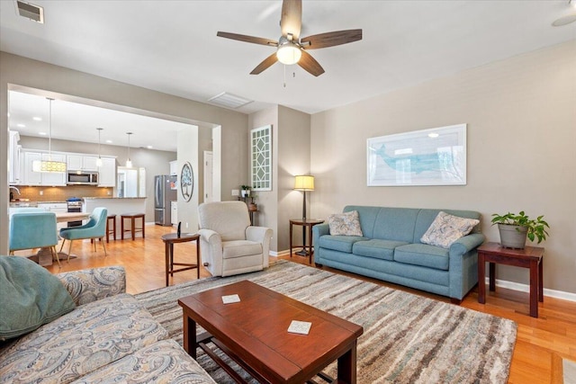 living area with light wood-type flooring, baseboards, visible vents, and ceiling fan