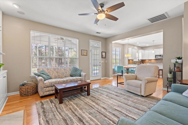 living area featuring light wood-style flooring, baseboards, visible vents, and ceiling fan