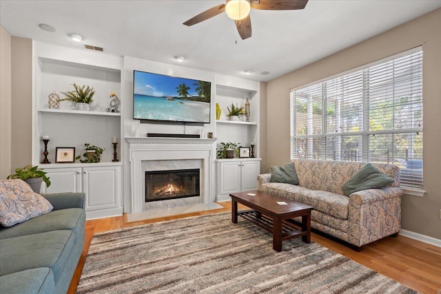 living room featuring visible vents, built in shelves, a premium fireplace, wood finished floors, and a ceiling fan