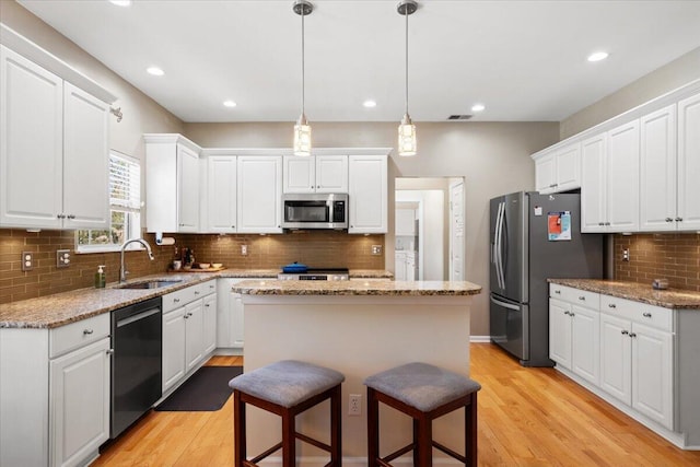 kitchen with a kitchen island, light wood-style flooring, appliances with stainless steel finishes, white cabinetry, and a sink