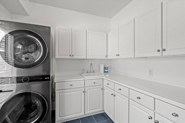 laundry room featuring dark tile patterned floors, cabinet space, stacked washer and clothes dryer, and a sink