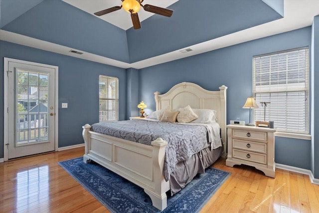 bedroom with a raised ceiling, access to outside, light wood-style floors, and visible vents