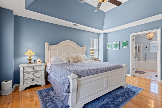 bedroom featuring visible vents, baseboards, vaulted ceiling, light wood-style floors, and ensuite bath