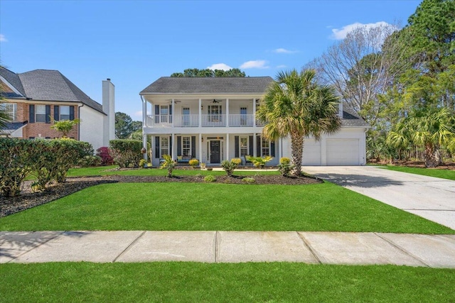 colonial house featuring covered porch, concrete driveway, a front yard, a balcony, and ceiling fan