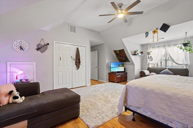 bedroom featuring a ceiling fan, visible vents, lofted ceiling, light wood-style flooring, and a closet