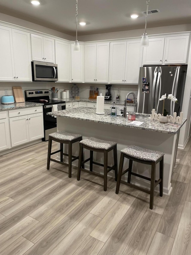 kitchen featuring hanging light fixtures, stainless steel appliances, an island with sink, light hardwood / wood-style floors, and a breakfast bar