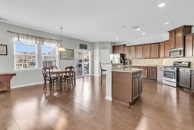 kitchen featuring appliances with stainless steel finishes, tasteful backsplash, light stone counters, pendant lighting, and an island with sink