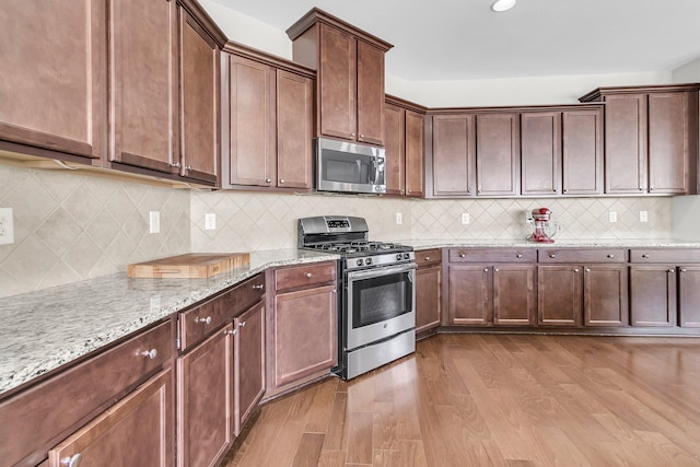 kitchen featuring decorative backsplash, light stone counters, light wood-type flooring, and stainless steel appliances