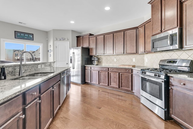 kitchen featuring light stone countertops, appliances with stainless steel finishes, dark brown cabinetry, sink, and light hardwood / wood-style flooring