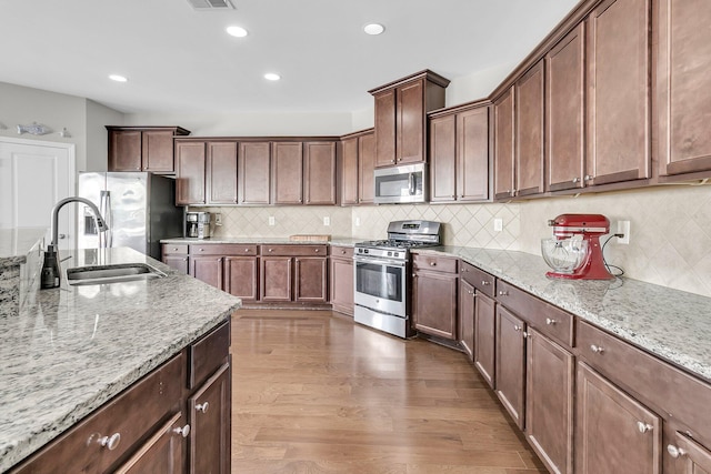 kitchen with hardwood / wood-style floors, sink, decorative backsplash, appliances with stainless steel finishes, and light stone counters