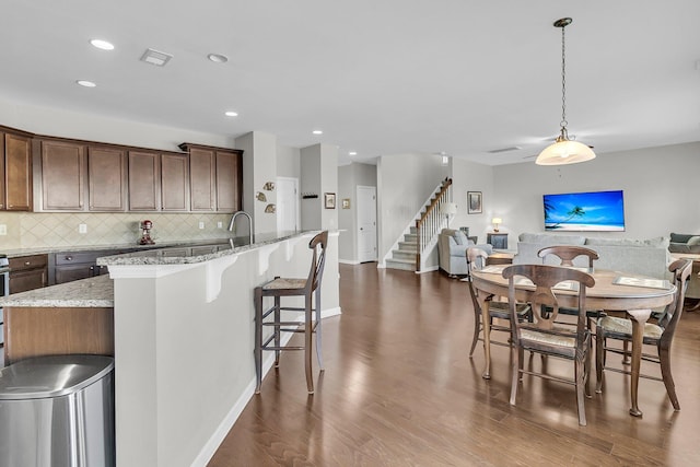 kitchen with pendant lighting, backsplash, light stone counters, and a kitchen island with sink