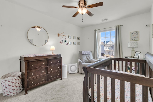 carpeted bedroom with ceiling fan and a crib