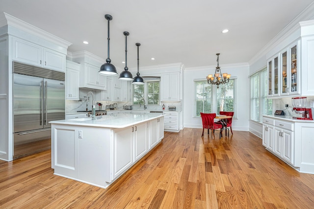 kitchen featuring glass insert cabinets, white cabinets, a center island with sink, and built in refrigerator