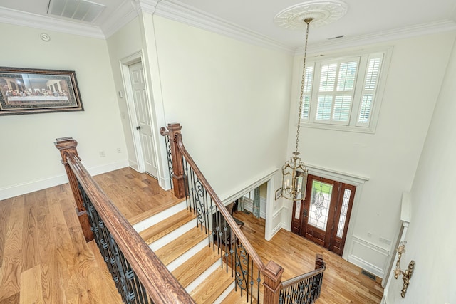 staircase featuring ornamental molding, wood finished floors, visible vents, and a healthy amount of sunlight