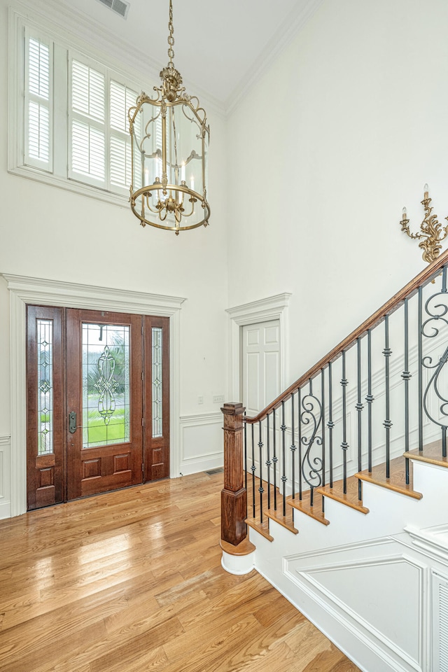 entryway featuring hardwood / wood-style floors, a towering ceiling, an inviting chandelier, and ornamental molding