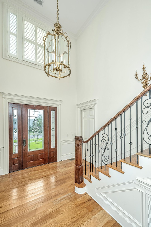 foyer entrance with light wood-style floors, a notable chandelier, stairway, and ornamental molding