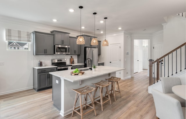 kitchen featuring a breakfast bar area, gray cabinetry, stainless steel appliances, a sink, and an island with sink