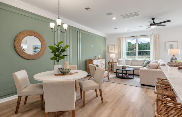 dining space featuring ornamental molding, visible vents, light wood-style flooring, and ceiling fan with notable chandelier