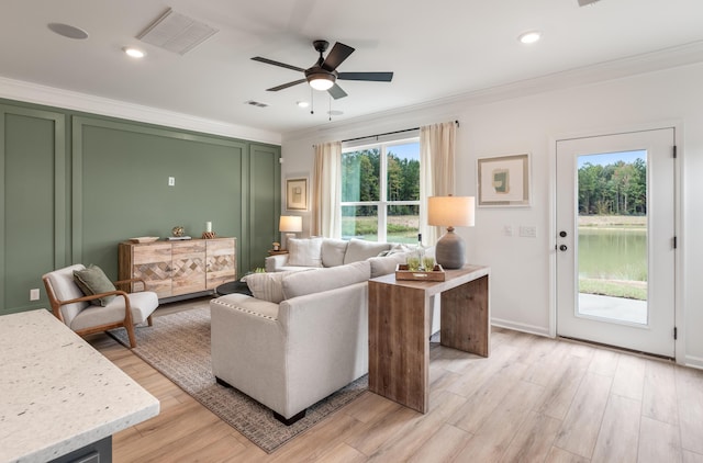 living room featuring ornamental molding, visible vents, light wood-style floors, and ceiling fan