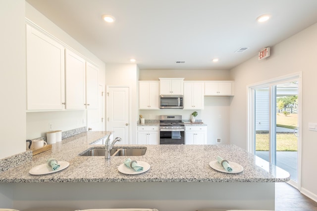 kitchen with white cabinets, sink, appliances with stainless steel finishes, light stone counters, and kitchen peninsula