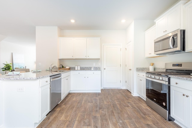 kitchen featuring light stone countertops, white cabinetry, stainless steel appliances, kitchen peninsula, and wood-type flooring