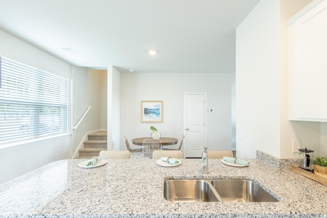 kitchen featuring white cabinets, light stone counters, and sink