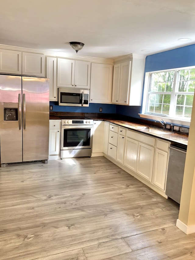 kitchen featuring light wood-type flooring, a sink, appliances with stainless steel finishes, and dark countertops