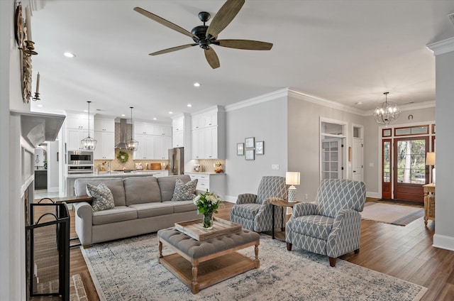 living room featuring wood-type flooring, ceiling fan with notable chandelier, and ornamental molding